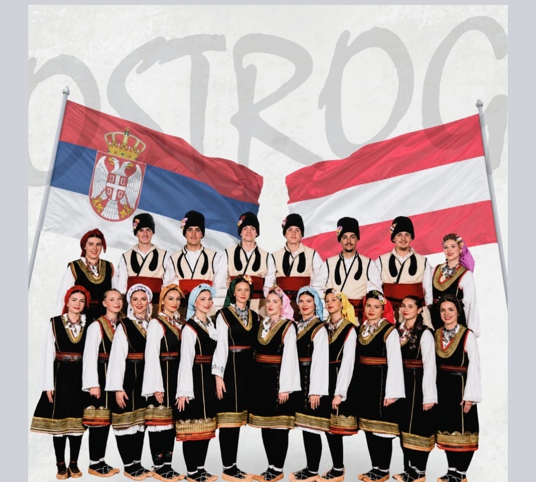 Die Mitglieder des KUD Ostrog Innsbruck in traditionellen Trachten vor serbischer und österreichischer Flagge
